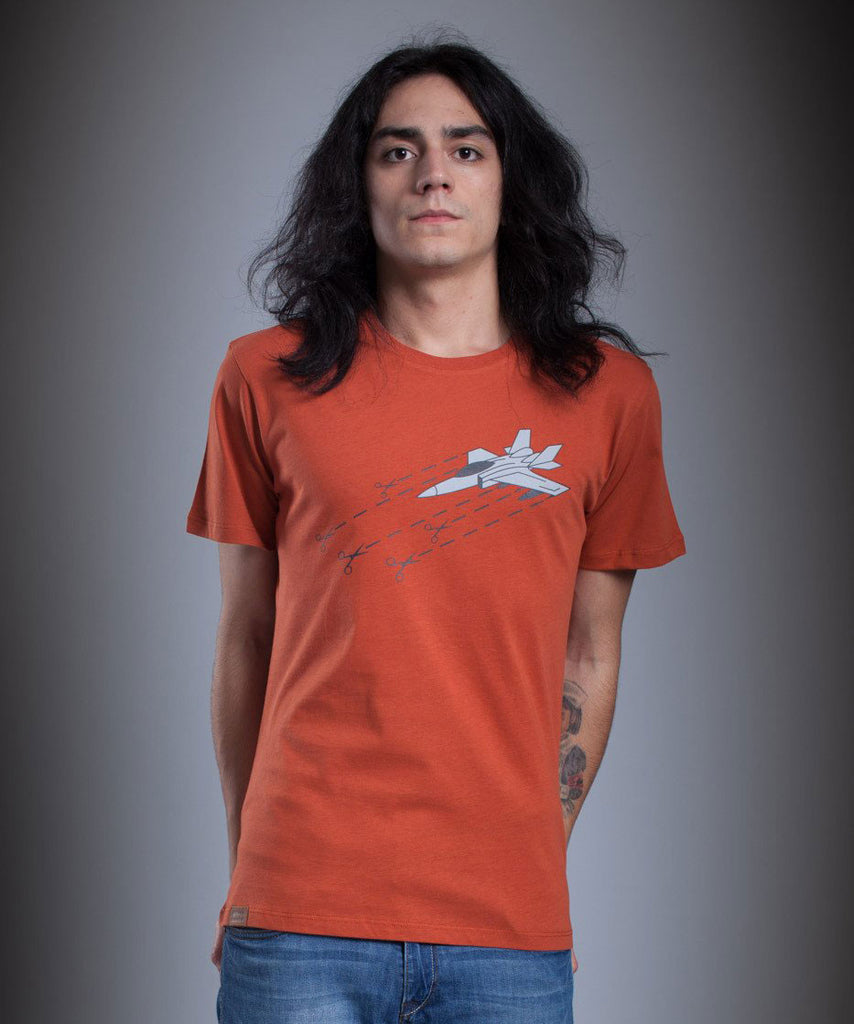 A guy is wearing Aponia Plane T-shirt in orange with the graphic of scissors cutting a fighter aircraft