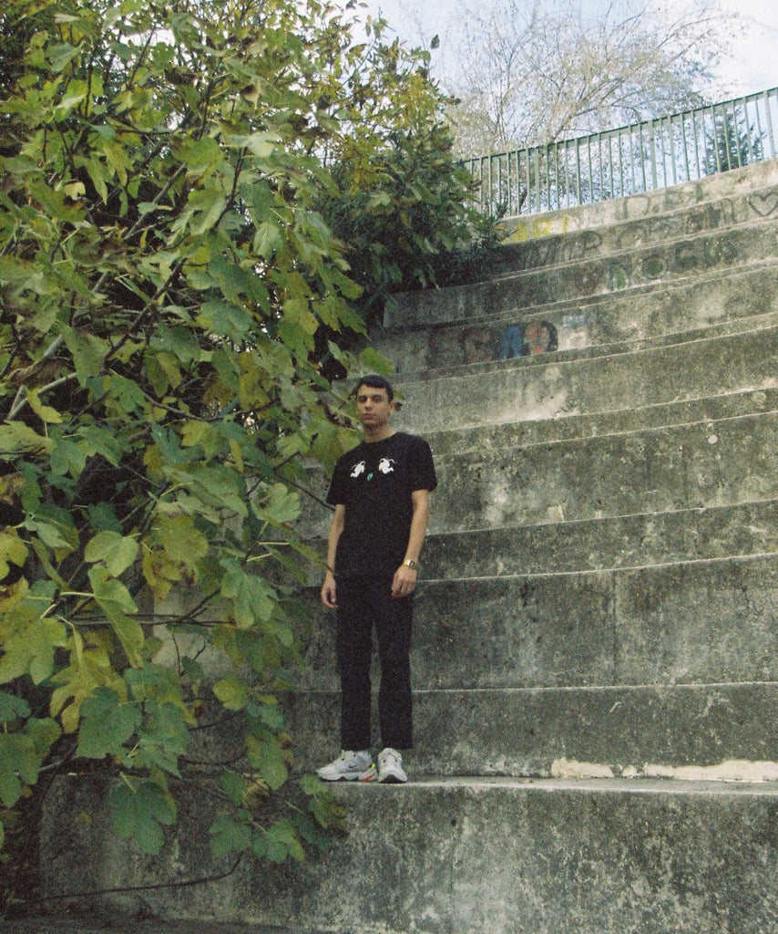 A guy standing on the stone stairs and wearing a astronaut  t-shirt with 2 astronauts holding arches